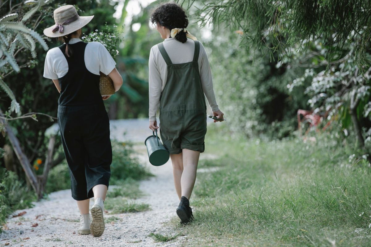 Two farmers walking down a garden path carrying tools and plants